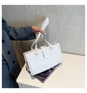 Detail einer weißen strukturierten Handtasche mit mattem Leder und silberner Schnalle