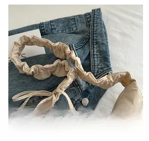 Detail of scrunchie handle and decorative bow on beige pleated nylon shoulder bag