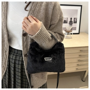 Détail du sac à main en fausse fourrure noire douce avec plaque en métal sur un pull