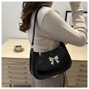 Glossy black underarm bag with a silver butterfly buckle worn on shoulder
