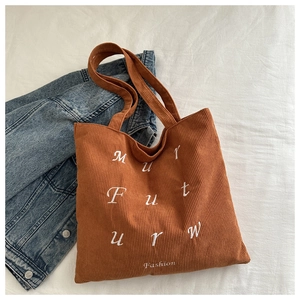 Detailed texture of brown corduroy tote bag with white letter embroidery and handles