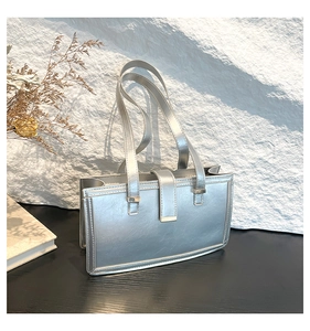 Detail einer silbernen Metallic-Umhängetasche mit minimalistischer Metallschnalle auf schwarzem Holz