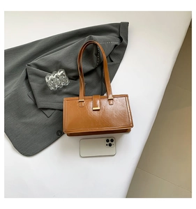 Braune glänzende Ledertasche mit goldener Schnalle neben Smartphone und grauem Blazer