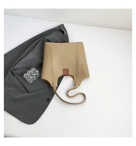 Minimalist beige leather tote bag with brown buckle detail on a grey suit background