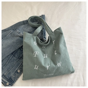 Close-up of light green corduroy tote bag featuring white artistic letter embroidery