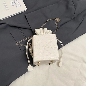 Detail of white lace-textured square bag with pearl pendant and metal chain strap