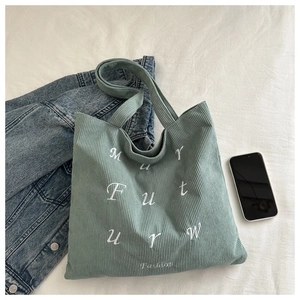 Close-up of mint green corduroy tote bag with white letter embroidery on a white fabric