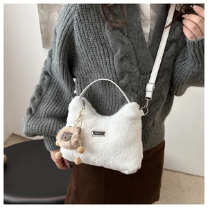 Détail d'un sac à bandoulière en peluche blanche avec badge sport et breloque ours