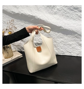 Detail of white leather tote bag with brown leather accent on a textured background