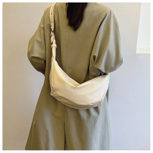 Detail of minimalist cream leather half-moon bag worn with olive trench coat