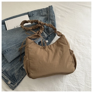 Detailed view of brown nylon cloud bag with pleated strap on denim jacket background
