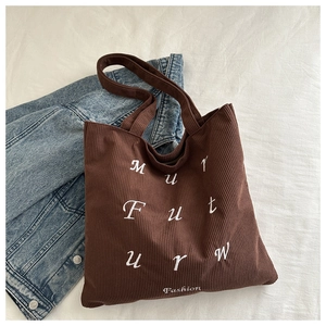 Close-up of brown corduroy tote bag with white letter embroidery on denim jacket