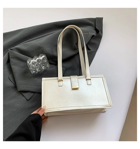 Detailansicht der cremefarbenen Tasche mit Gold-Schnallen auf grauem Blazer-Hintergrund