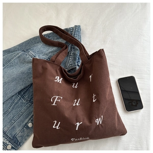 Detailed close-up of dark brown corduroy tote bag with white letter embroidery