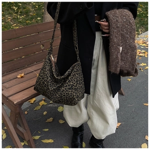 Close-up of leopard print hobo bag with gold zipper on a wooden park bench in autumn