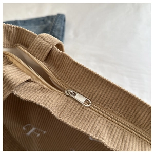 Detail of khaki corduroy tote bag showing metal zipper closure and white letter embroidery