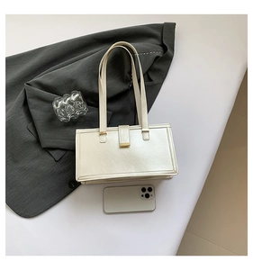 Detail der beigen Leder-Schultertasche mit Goldverschluss auf einem grauen Sakko