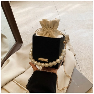 Detail view of pearl handle and gold chain on black textured drawstring bucket bag