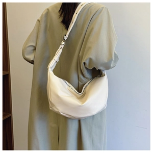 Detail of soft cream leather crescent bag featuring a wide shoulder strap and silver rivets
