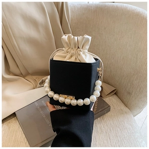 Detail of cube crossbody bag with faux pearl handle and gold chain strap on a book