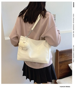 Detail of white leather tote bag with silver chain straps and a plush charm
