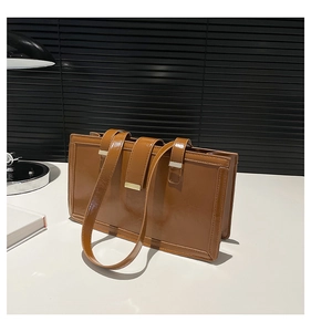 Braune rechteckige Handtasche aus glänzendem Leder mit Metallschnalle auf Schreibtisch