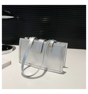 Nahaufnahme einer silbernen rechteckigen Handtasche mit goldenen Schnallen auf weißem Tisch