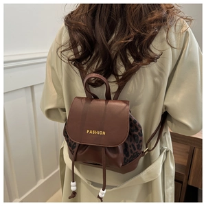 Detail of a brown leopard print backpack with gold fashion logo and drawstring beads