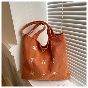Close-up of orange corduroy tote bag with white embroidered letters and rich texture