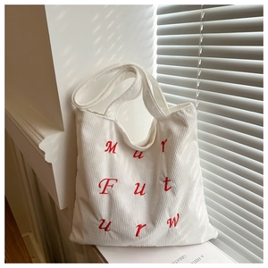 Close-up of white corduroy tote bag featuring red embroidered letters and ribbed texture