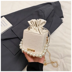 Detailed view of cream lace bucket bag with pearl handle and golden chain strap