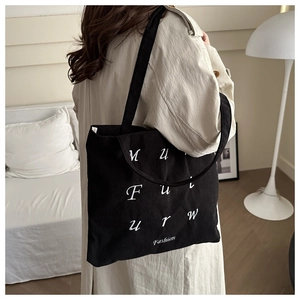 Close-up of black corduroy tote bag with white letter embroidery on beige trench coat