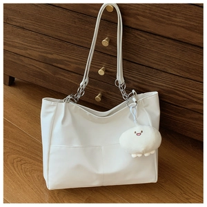 Close-up of white tote bag with metal chain strap and cute plush charm on wood cabinet