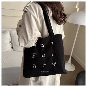 Detail of black corduroy tote bag with white embroidery worn by a model in a modern room