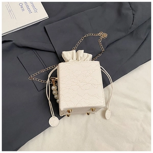 Detail of white lace handbag featuring gold chain, drawstring closure and pearl charm