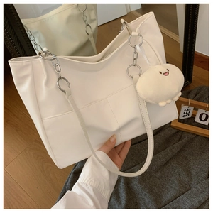 Detailed view of white leather tote bag featuring chain handle and cute plush charm