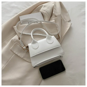 Mini white handbag size comparison with smartphone on beige blazer background