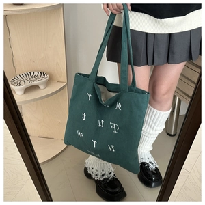 Close-up of dark green corduroy tote bag featuring white letter embroidery and soft texture