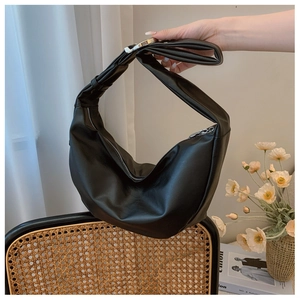 Detail of a black leather half-moon shoulder bag with zipper on a wicker chair