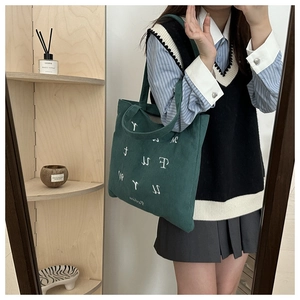 Detail of dark green corduroy tote bag featuring white embroidered letters and handle