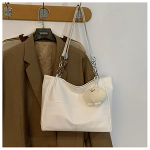 Close-up of white tote bag with metal chain strap and cute plush smiley face charm