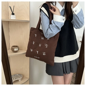 Detail of dark brown corduroy tote bag featuring white embroidered letters and handle