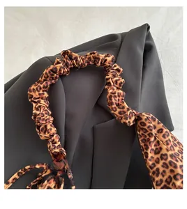 Close-up of leopard print canvas bag featuring retro pleated handles on a black blazer