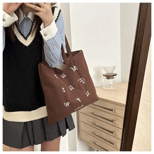 Close-up of brown corduroy tote bag featuring white letter embroidery and a square cut