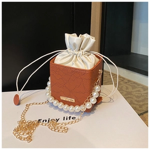 Macro detail of brown leather bag with lace texture, pearl handle and gold chain strap