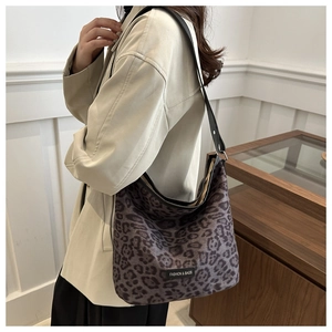 Close-up of leopard print hobo bag featuring wide black strap and fashion label on a model