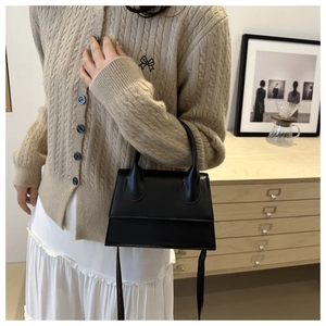 Classic black matte leather trapezoid handbag worn by model in a warm indoor setting