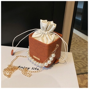 Detail of caramel bucket bag featuring lace texture, pearl handle, and gold chain strap