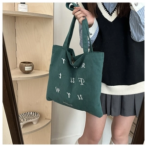 Close-up of emerald green corduroy tote bag featuring artistic white letter embroidery