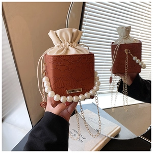 Detail der braunen Spitzen-Box-Tasche mit Perlengriff und goldener Kettenverzierung